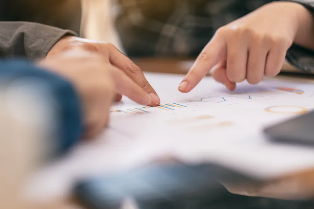 Hands pointing at colorful bar graphs and charts on paper.