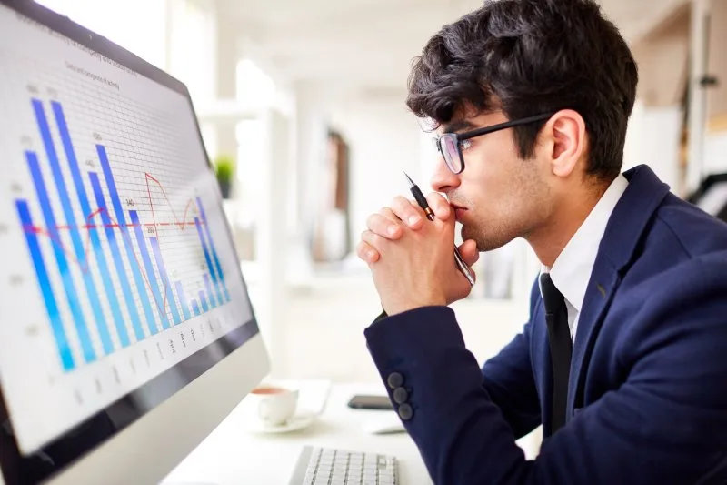 Financial advisor sitting at a desk in front of a large monitor screen analyzing digital marketing data.