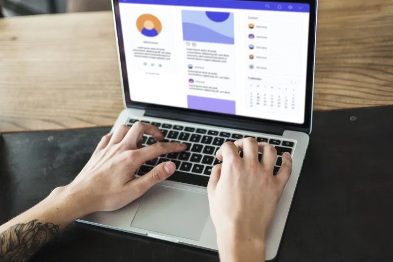 Competitor ad copy paid social research, hands typing on laptop reviewing social dashboard, posts, calendar.