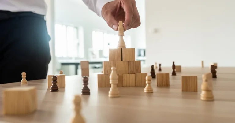 Businessman stacking chess pieces on a wooden block pyramid symbolizing website content hierarchy and strategic SEO structure.