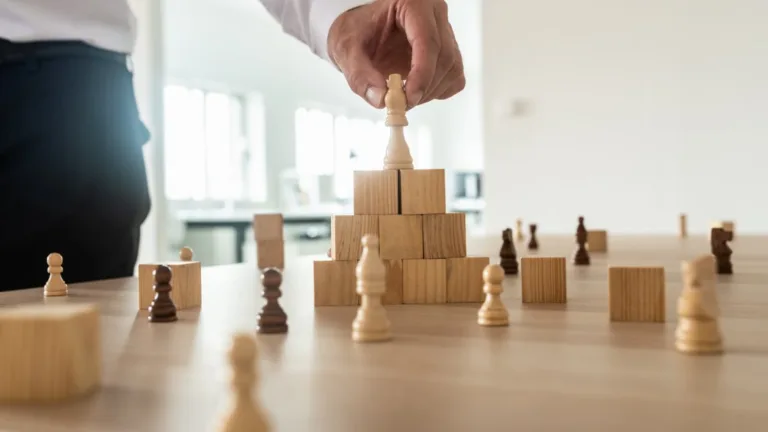 Businessman stacking chess pieces on a wooden block pyramid symbolizing website content hierarchy and strategic SEO structure.