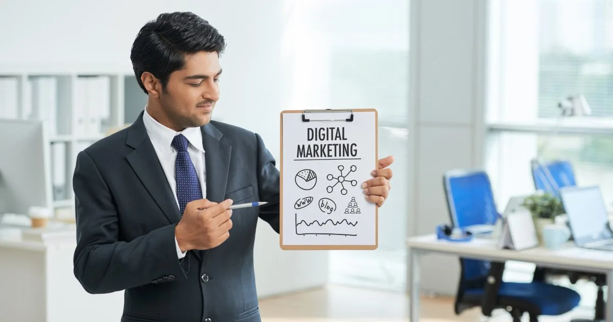 Financial advisor standing in a large office holding and pointing to a clipboard that reads, “Digital Marketing.”