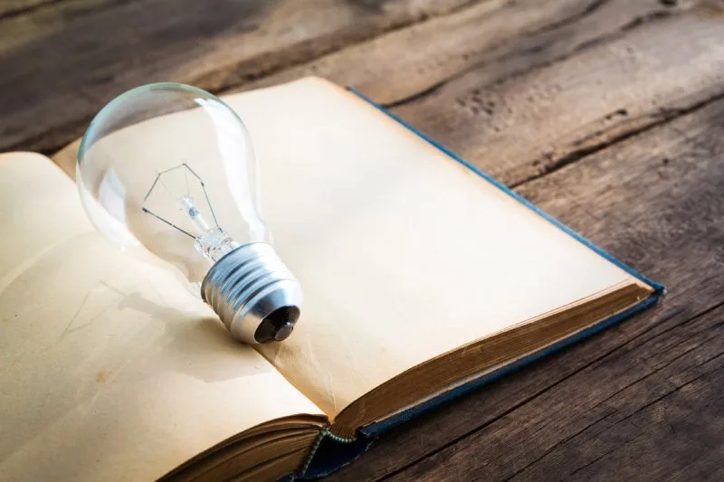 Open book with a light bulb resting on the pages, representing topic cluster knowledge and content authority building
