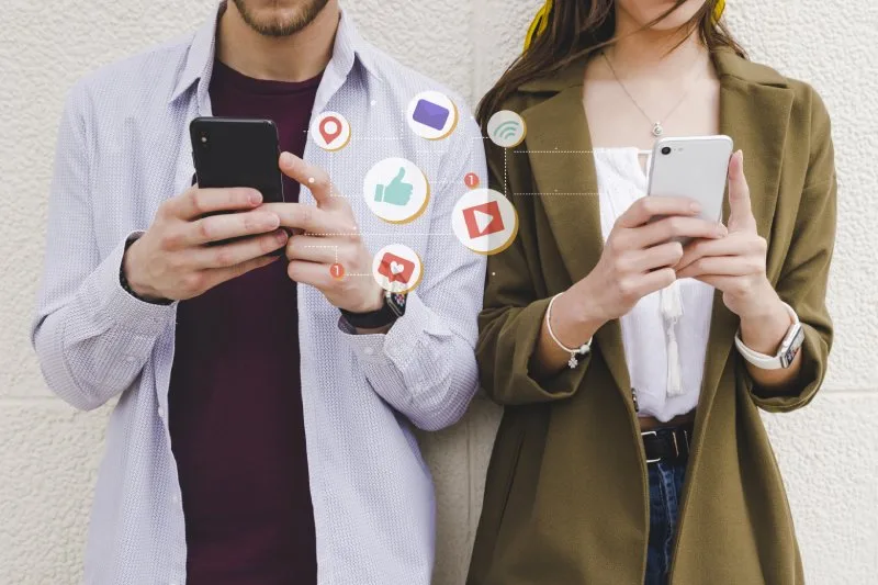 Two people on smartphones with social media icons, representing paid social advertising campaigns.