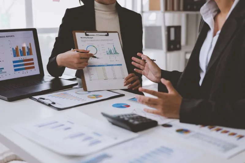 Two financial professionals reviewing business performance reports and analytics charts during a strategy meeting. 