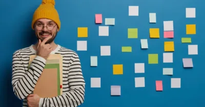 Content strategist holding notebooks and smiling next to a wall of sticky notes, representing topic cluster planning and content organization