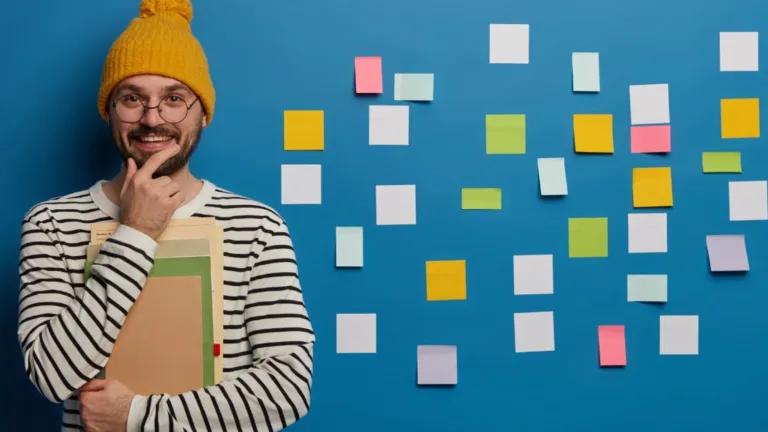 Content strategist holding notebooks and smiling next to a wall of sticky notes, representing topic cluster planning and content organization