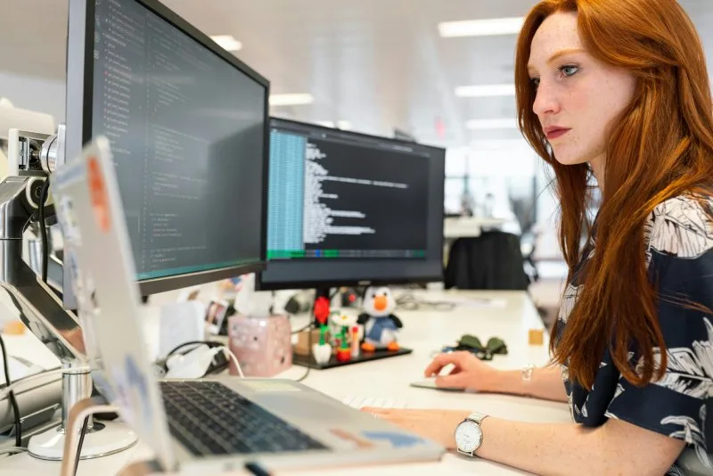 Woman working on multiple monitors with code, representing website optimization and technical SEO.