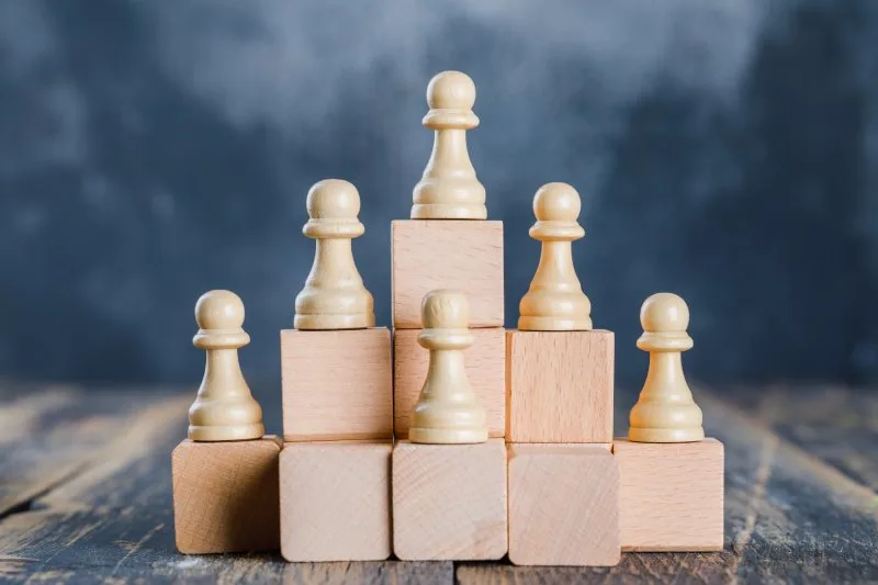 Chess pawns arranged on stacked wooden blocks forming a pyramid showing visual website content hierarchy.
